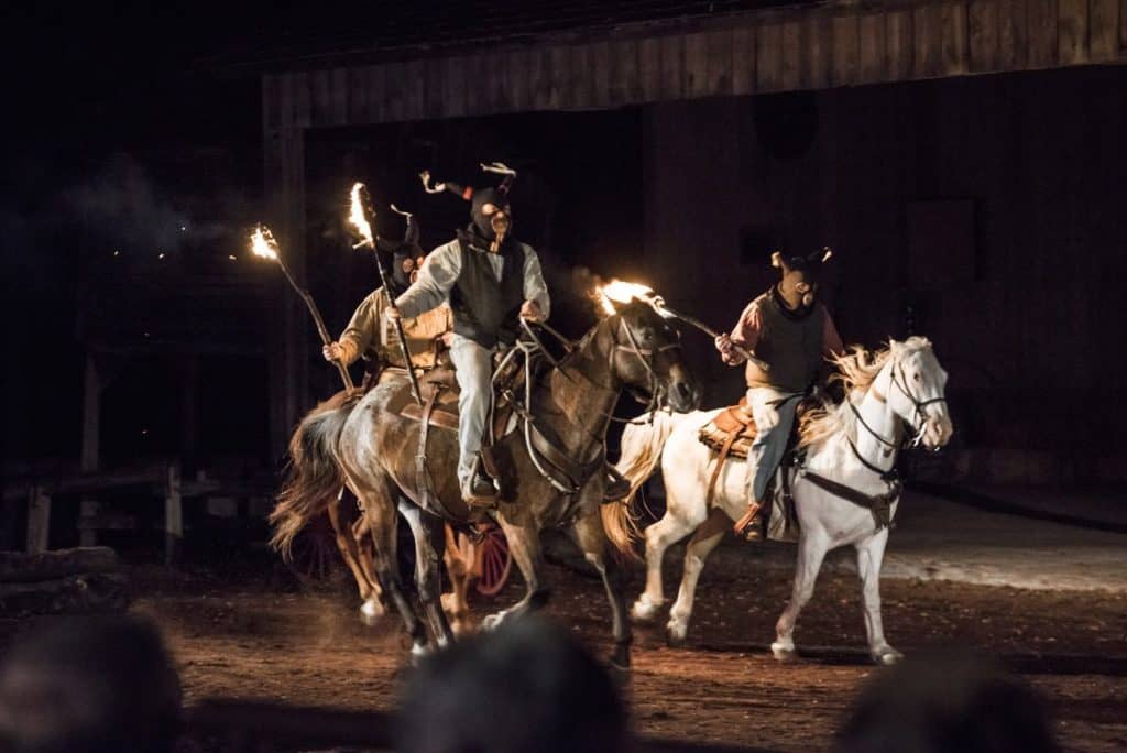 Men in masks holding torches on horseback